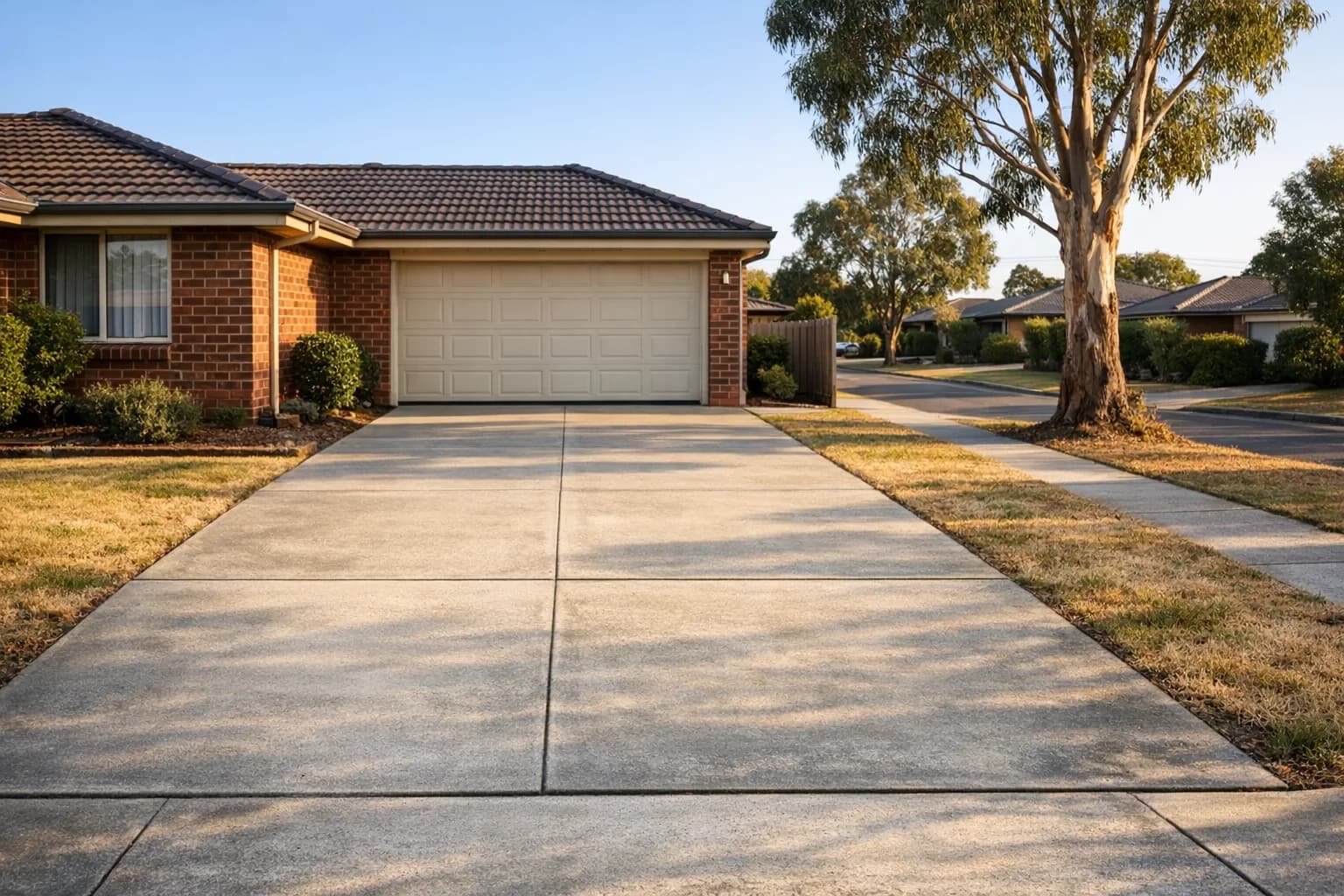 Suburban Australian brick home with a double garage and concrete driveway in afternoon light